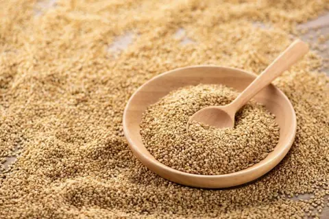 Un bol en bois rempli de graines de sésame, avec une cuillère en bois. Les graines de sésame bienfait sont une source de nutriments.