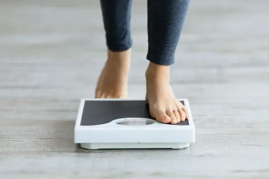 Pieds nus sur une balance, scrutant une possible perte de poids inexpliquée.