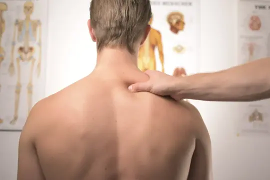 Main d'un thérapeute palpant le dos d'un homme, cherchant la cause d'une douleur intense bas du dos. Anatomie visible en arrière-plan.