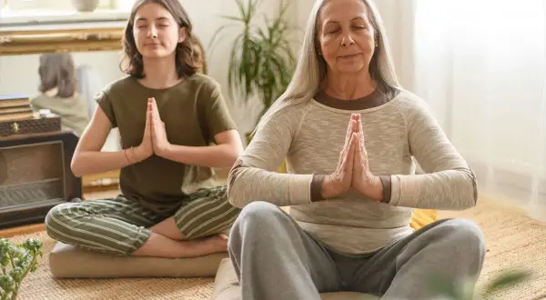 Deux femmes méditent, une jeune et une plus âgée. La méditation peut aider à gérer le stress et la prise de poids liée à la préménopause.