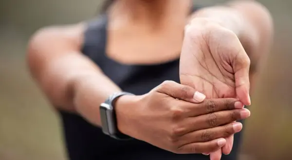Une femme étire son poignet, peut-être pour soulager une douleur poignet externe après un effort.