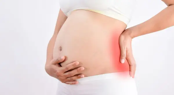 Femme enceinte tenant son ventre, une zone rouge sur le côté indique une douleur au fessier en fin de grossesse.