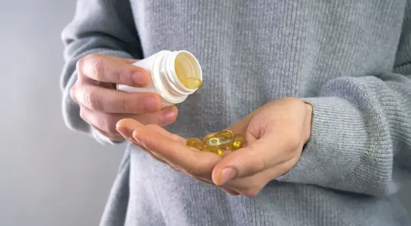 Main tenant une capsule d'huile de poisson dans sa main, prêt à prendre son complément. Avis sur les oméga 3.