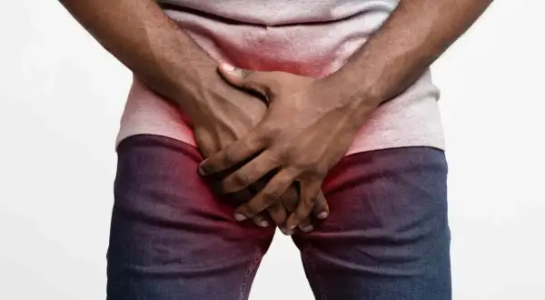 Homme tenant ses mains sur son pubis, zone rouge indiquant une douleur ou une gêne.