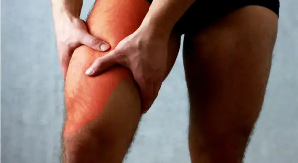Main gauche tenant la cuisse droite, marquée d'une zone rouge symbolisant une douleur haut de la cuisse.