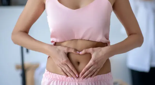 Femme faisant un cœur avec ses mains sur son ventre, soulageant un tiraillement bas ventre.