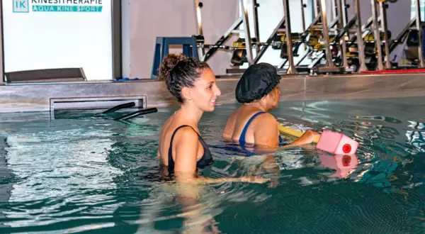 Une kinésithérapeute guide une patiente dans l'eau, utilisant des exercices aquatiques comme remède miracle pour capsulite.