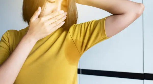 Une femme se couvre le nez, gênée par sa transpiration qui sent fort depuis peu. Une auréole de sueur est visible sous son bras.