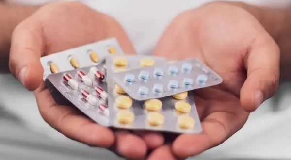 Mains tenant plusieurs plaquettes de pilules, dont des gélules rouges et blanches, des comprimés bleus et des comprimés jaunes. Que prendre avec des antibiotiques ?