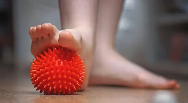 Un pied utilise une balle rouge texturée pour soulager une tendinite sous le pied.