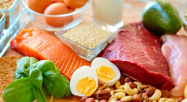Assortiment d'aliments riches en protéines pour personnes âgées : saumon, bœuf, poulet, œufs, noix, épinards, avocat, quinoa et lait.