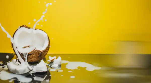 Un coco ouvert éclabousse du lait blanc sur un fond jaune vif, évoquant les nombreux lait de coco bienfaits.