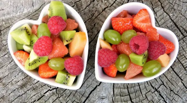Deux bols en forme de cœur remplis de fruits non acides : fraises, framboises, kiwis, raisins, melon et pamplemousse.