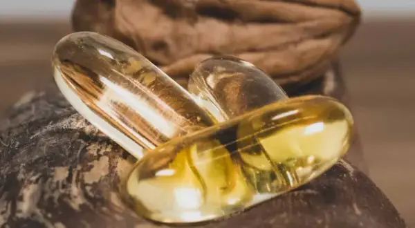 Trois capsules d'oméga 3 dorées reposent sur une noix. Quand prendre oméga 3 pour un bien-être optimal ?