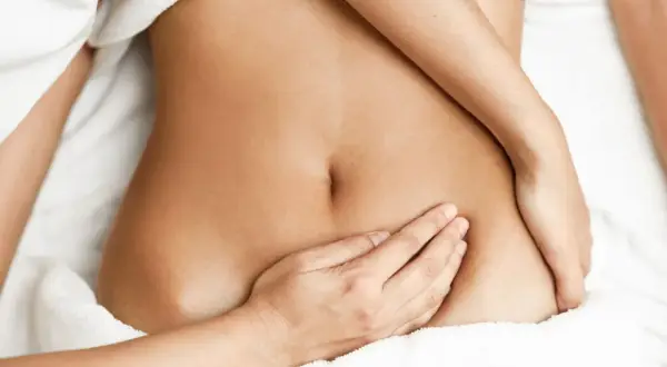 Main d'une femme posée sur son ventre, soulageant une douleur bas ventre gauche.