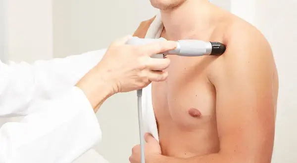 Thérapeute appliquant des ondes de choc radiales sur l'épaule d'un patient pour soulager la douleur.
