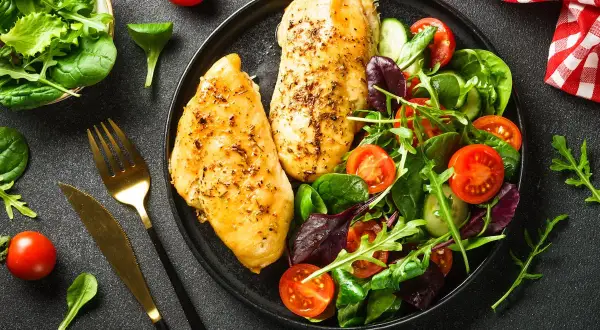 Deux blancs de poulet grillés avec une salade fraîche. Un repas sain, idéal pour savoir quels aliments éviter quand on a du cholestérol.