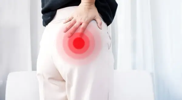 Une femme se tient le fessier droit, marqué par des cercles rouges, suggérant une douleur. La signification de cette douleur fessier droit peut varier.