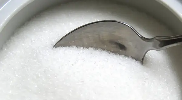 Une cuillère dans un bol de sucre blanc, rappelant les dangers du cholestérol, du sucre ou du sel pour la santé.