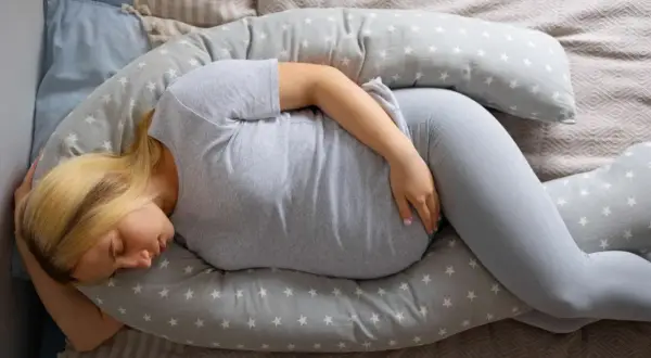Femme enceinte dormant sur un coussin de maternité, cherchant le confort face aux douleurs ligamentaires de grossesse.