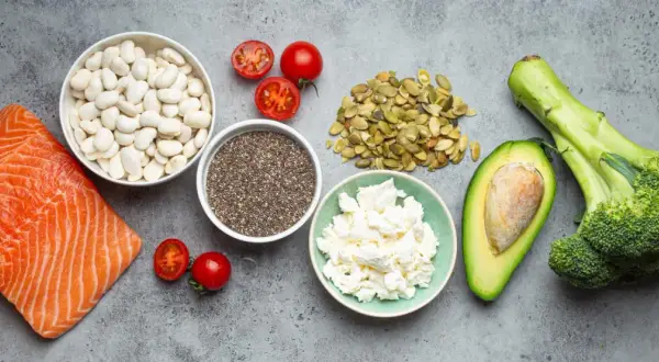 Saumon, haricots blancs, tomates, graines de chia, fromage blanc, avocat et brocoli sur fond gris.