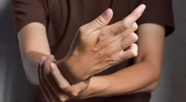 Main tenant une main, l'autre main se tient le poignet, suggérant des symptômes de fonte musculaire.