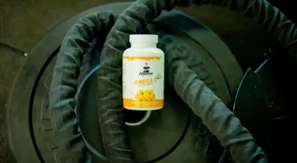 Bouteille d'oméga 3 sur des poids de musculation, idéale pour le bien-être, matin ou soir.