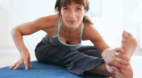 Femme en tenue de sport s'étirant sur un tapis bleu. Elle semble ressentir une douleur au muscle pectiné.