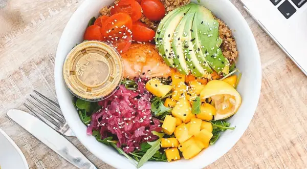 Un bol coloré avec saumon, avocat, tomates, mangue et chou rouge. Une assiette saine pour savoir comment faire baisser son taux d'insuline naturellement.