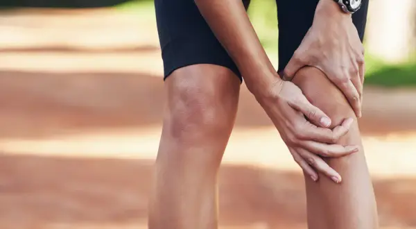 Une athlète se tient le genou, peut-être une douleur au ligament croisé du pied.
