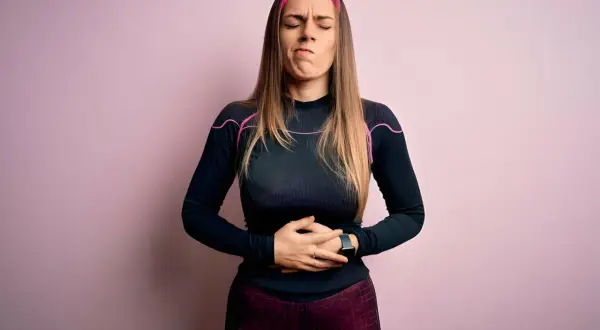 Femme en tenue de sport, mains sur le ventre, grimace de douleur. Elle a des douleurs de règles mais pas de règles.