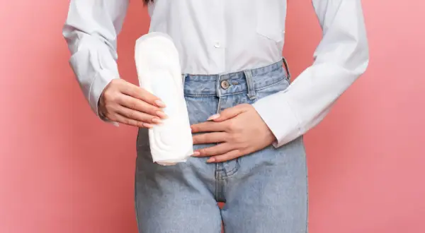 Une femme tient une serviette hygiénique, le ventre douloureux, symbolisant la douleur de règle sans règle.