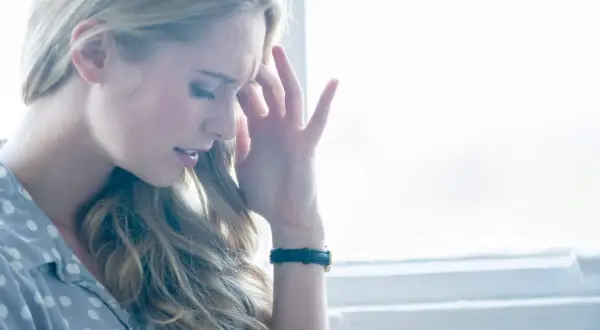 Femme blonde se tenant la tempe, le regard baissé, l'air de souffrir d'une sensation de pression dans la tête et vertige.