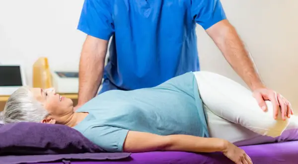 Un kinésithérapeute aide une femme à faire un exercice pour soulager sa tendinite fessière.