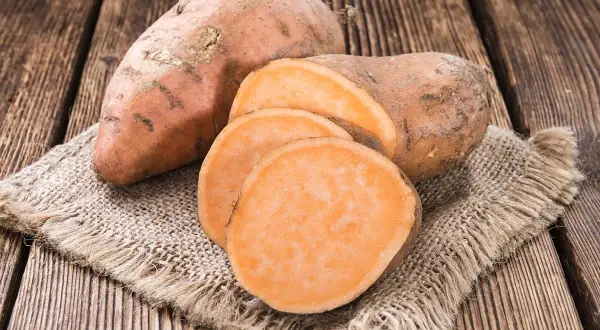 Patates douces entières et tranchées sur une toile de jute. Un aliment sain, faible en calories, parfait pour une alimentation équilibrée.