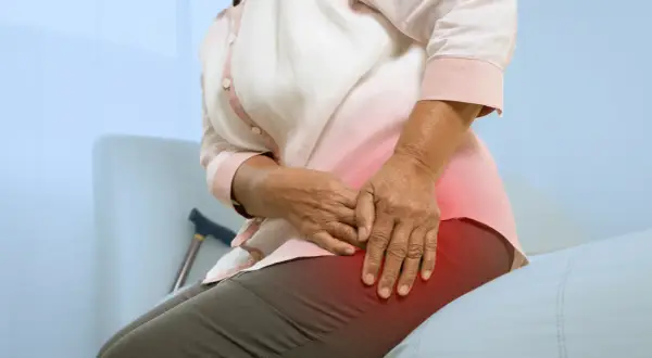 Une personne âgée ressent une douleur à la hanche, peut-être due à une ancienne blessure de course à pied. Une canne est visible à proximité.