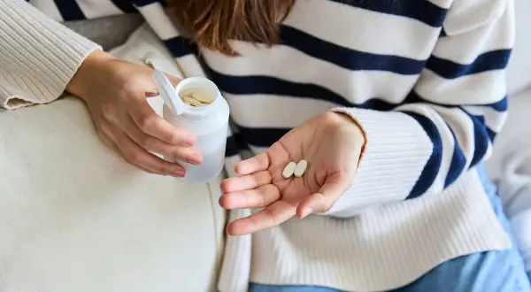 Une femme tient des comprimés dans sa main, peut-être pour lutter contre la fatigue. Le collagène est une option.