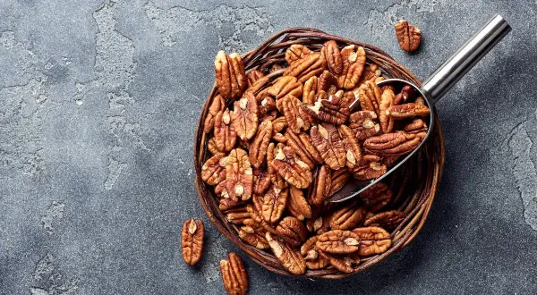 Un panier rempli de noix de pécan, une cuillère métallique en extrait. Savourez les noix de pécan, un concentré de bienfaits pour la santé.