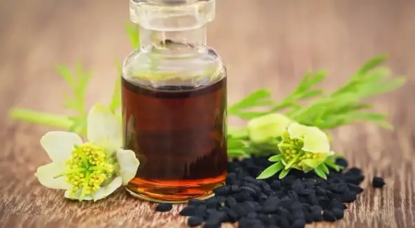 Flacon d'huile de nigelle, graines noires et fleurs. Un remède naturel pour la fonte musculaire.