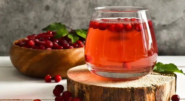 Verre de jus de cranberry, fruit réputé pour aider contre l'infection urinaire. Baies rouges dans un bol en bois.