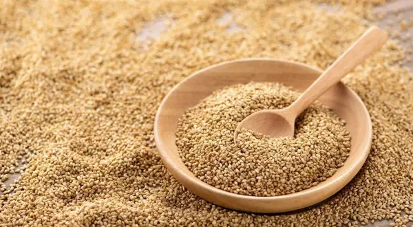Un bol en bois rempli de graines de sésame, avec une cuillère en bois. Les graines de sésame bienfait sont une source de nutriments.