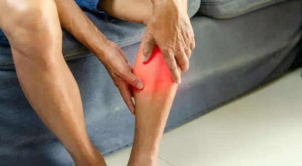 Main tenant sa jambe, une personne ressent une douleur vive, se demandant combien de temps d'arrêt de travail pour une déchirure musculaire.