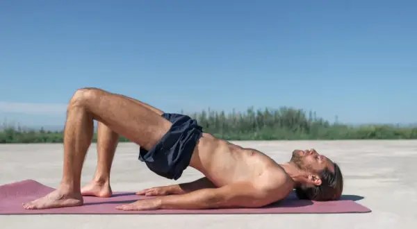 Homme en posture de pont sur un tapis, explorant comment trouver le périnée chez l'homme.