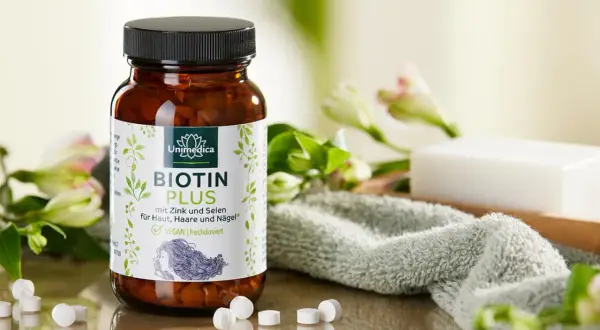 Flacon de Biotin Plus, une réponse à quelle vitamine pour les ongles, avec des fleurs et une serviette.