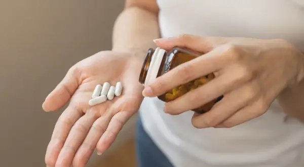 Main tenant une pilule dans sa paume, une personne verse des capsules d'un flacon. Une cure de vitamine D pour le bien-être.
