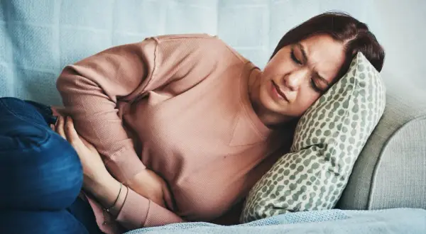 Femme souffrant de SPM, se tenant le ventre sur un canapé. Combien de temps avant que la douleur ne passe ?
