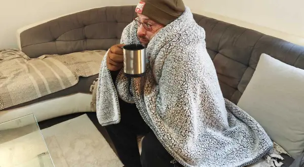 Un homme emmitouflé dans une couverture, tenant une tasse chaude, se demande pourquoi j'ai froid alors qu'il fait chaud.