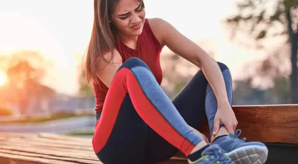 Une coureuse s'assoit sur un banc, se tenant la cheville avec une expression de douleur. La douleur à la cheville après la course à pied peut être débilitante.
