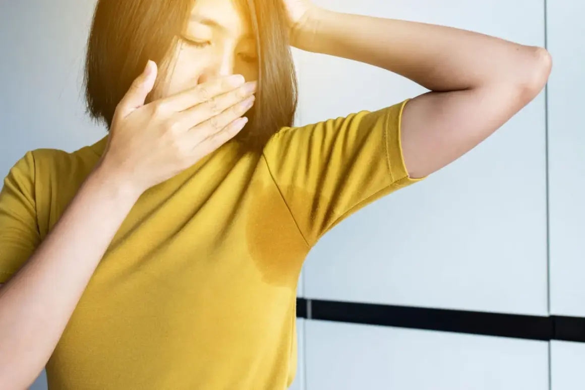 Une femme se couvre le nez, gênée par sa transpiration qui sent fort depuis peu. Une auréole de sueur est visible sous son bras.