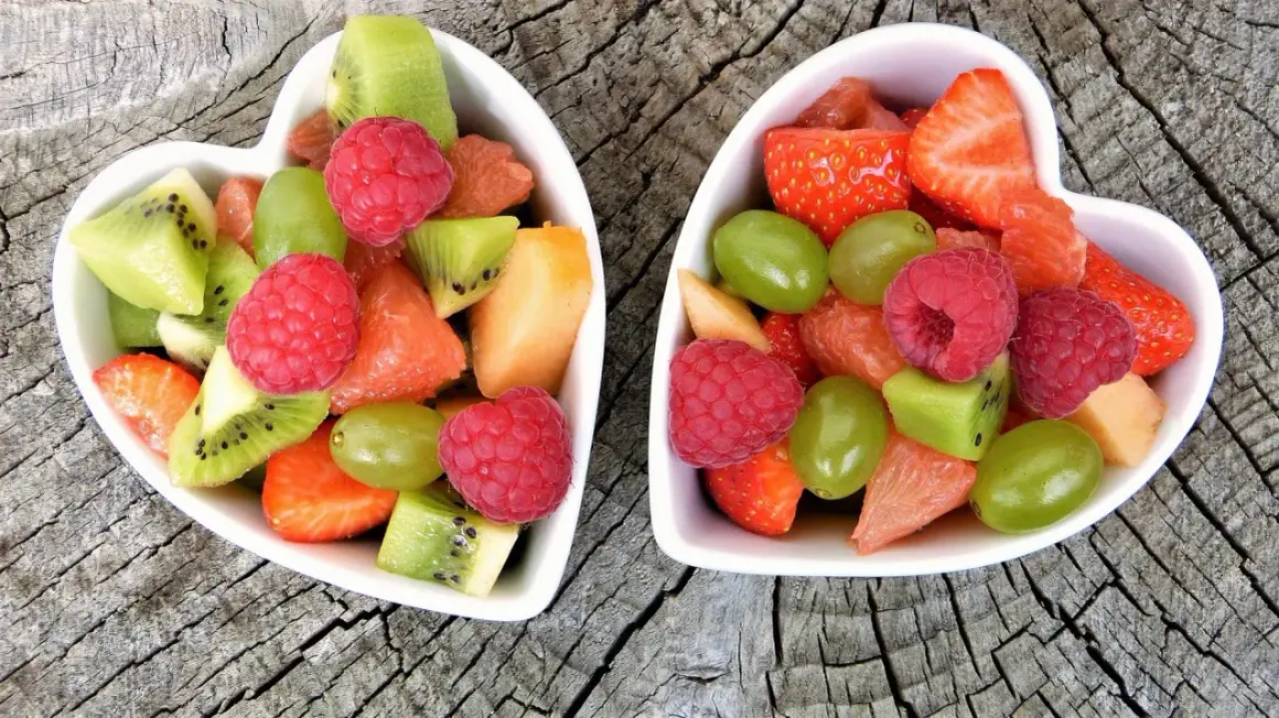 Deux bols en forme de cœur remplis de fruits non acides : fraises, framboises, kiwis, raisins, melon et pamplemousse.